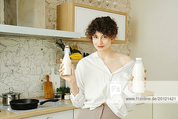 Cheerful woman holds bottle with milk and cream in both hands
