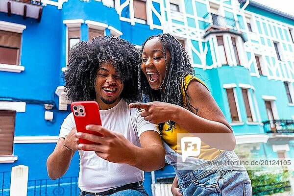 Afrikanische Freunde  die mit überraschtem Gesichtsausdruck auf ein Handy zeigen  das neben blauen bunten Häusern in der Stadt steht