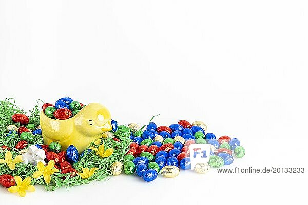 Chocolate eggs and a decorative chick surrounded by artificial grass as a festive decoration  white background