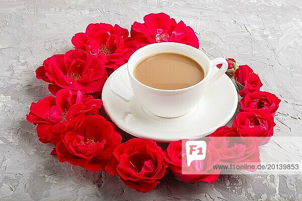 Rote Rosenblüten in einer Spirale und eine Tasse Kaffee auf einem grauen Betonhintergrund. Morgen  Frühling  Mode Komposition  Seitenansicht  Nahaufnahme