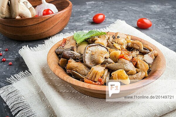 Fried oyster mushrooms with tomatoes in wooden plate on black concrete background. side view  close up