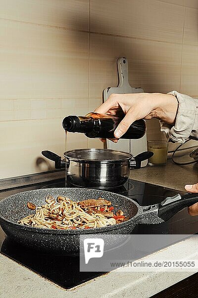 Unrecognizable woman pouring oyster sauce into noodles in a frying pan