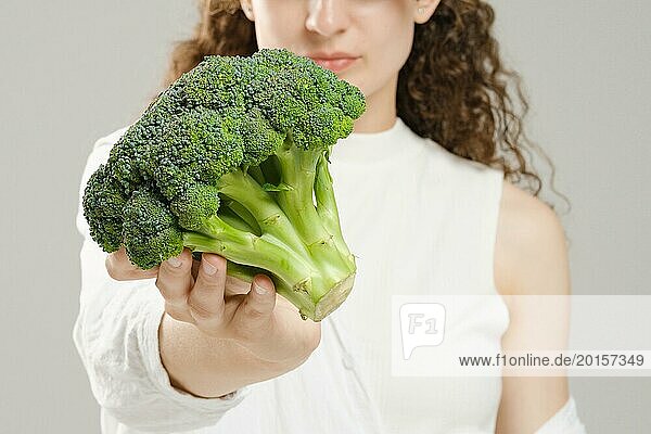 Unbekannte Frau hält Brokkoli in ihrer ausgestreckten Hand  Fokus auf den Vordergrund