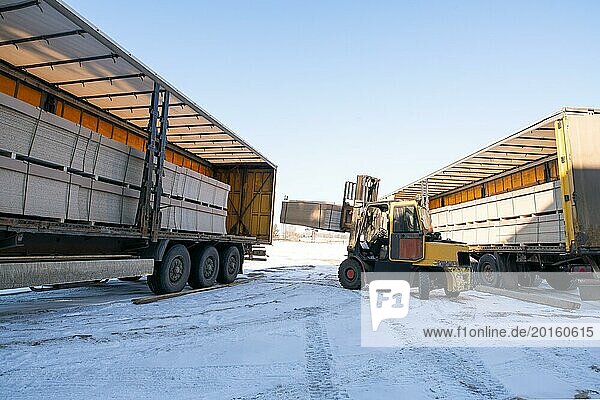 Industrial machinery with trucks and tractor with heavy packages parked on snowy road in winter time