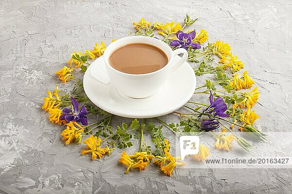 Gelbe und blaue Blumen in einer Spirale und eine Tasse Kaffee auf einem grauen Betonhintergrund. Morninig  Frühling  Mode Zusammensetzung. Seitenansicht  Nahaufnahme
