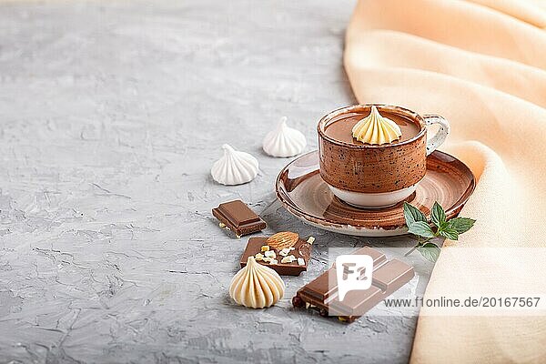 Tasse heiße Schokolade und Milchschokoladenstückchen mit Mandeln auf grauem Betonhintergrund mit orangefarbenem Textil. Seitenansicht  Kopierraum