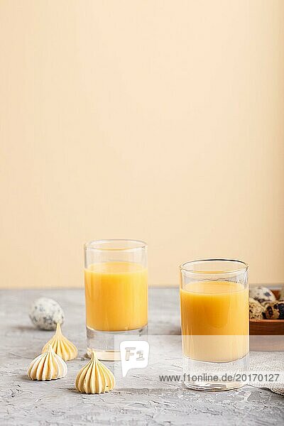 Süßer Eierlikör im Glas mit Wachteleiern und Meringues auf grauem und orangefarbenem Hintergrund. Seitenansicht  Kopierbereich