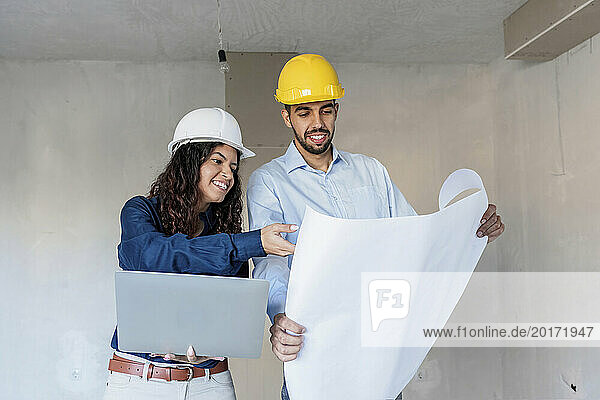 Happy architects discussing with blueprint and laptop at site