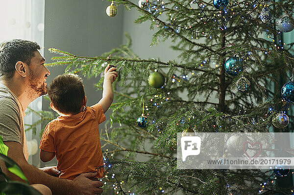 Boy decorating Christmas tree with father at home