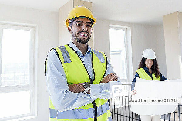 Smiling confident architect with colleague in background at site