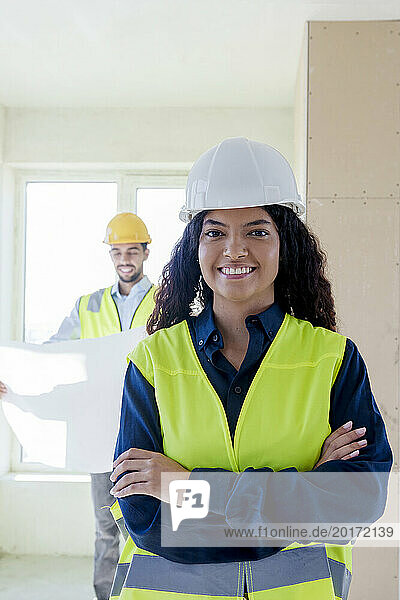 Smiling young architect standing with arms crossed at site