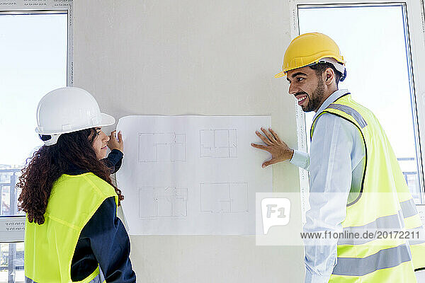 Architects discussing over blueprint on wall at site