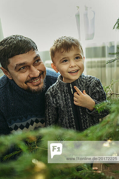 Smiling man looking at Christmas tree with son at home