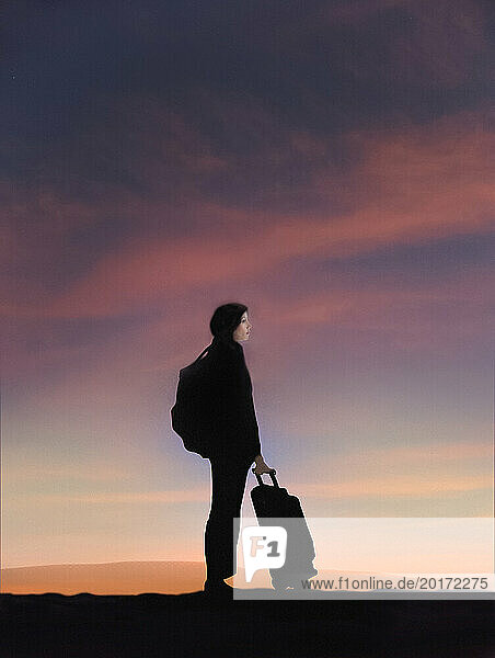 Young woman traveling with luggage at sunset