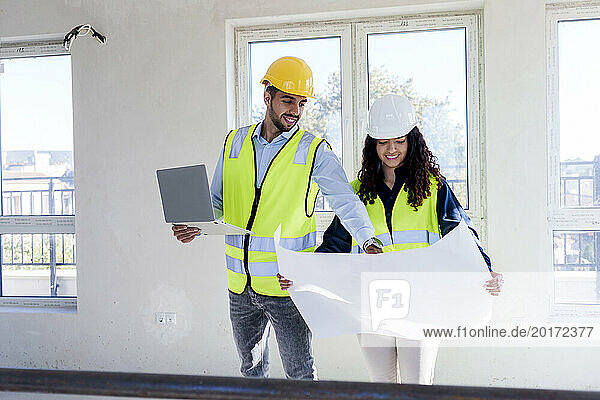 Smiling architect discussing over blueprint with colleague at site