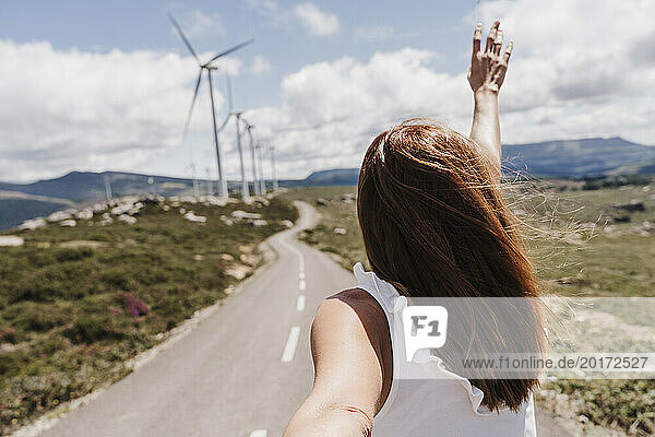 Spain  Madrid  Back of woman reaching toward clouds in front of wind farm