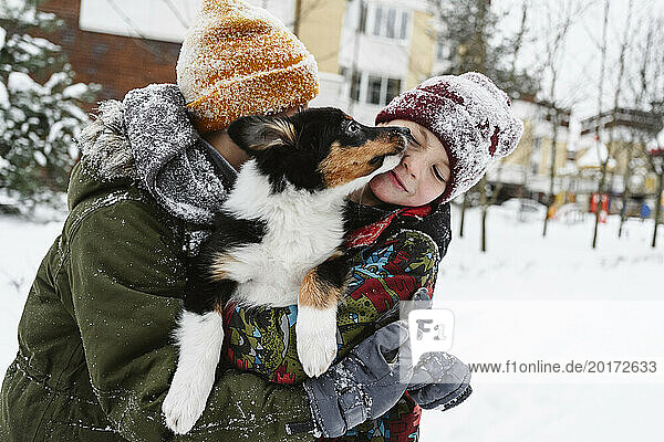 Playful siblings holding dog together in arms on snow