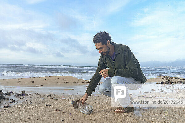 Man picking up plastic bottle on coastline at beach