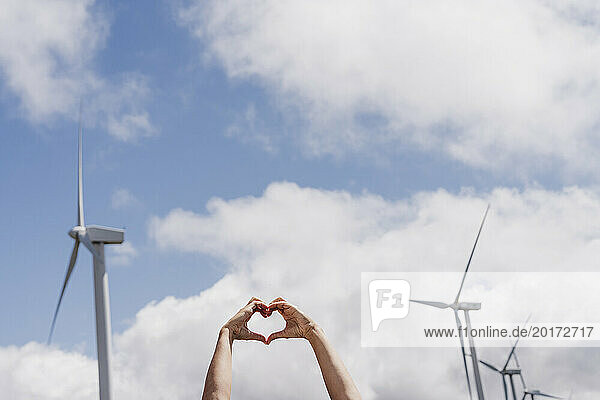 Spain  Madrid  Hands of woman making heart shape against clouds and wind farm turbines