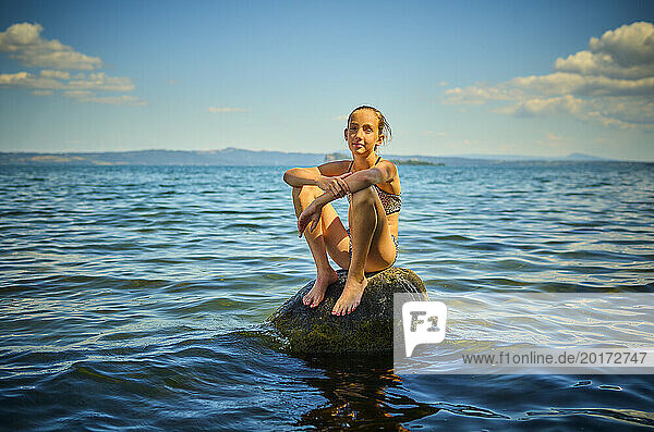 Girl sitting on rock in lake Bolsena  Italy