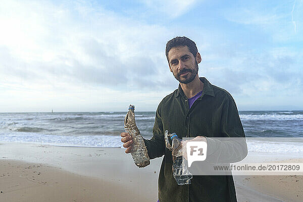 Man standing with plastic bottles under cloudy sky at beach