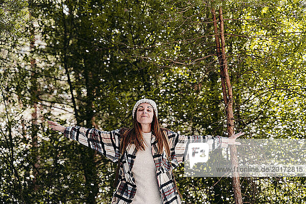 Carefree woman standing with arms outstretched amidst trees in forest