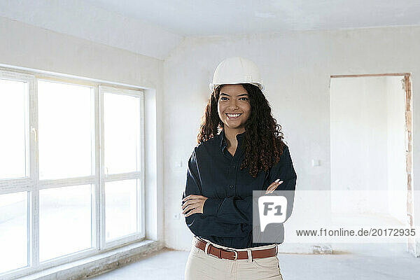 Smiling architect with arms crossed standing at construction site
