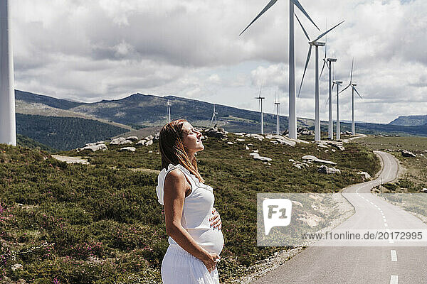 Spain  Madrid  Pregnant woman standing on roadside in front of wind farm turbines