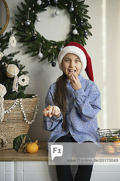 Girl wearing Santa hat and eating oranges at home