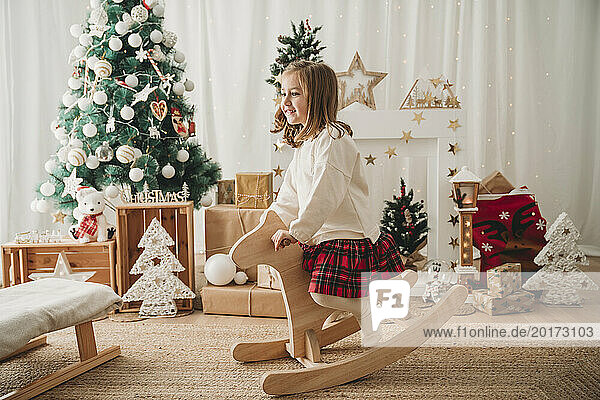 Happy girl sitting on wooden rocking horse at home