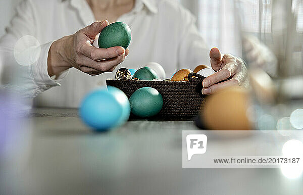 Woman keeping green egg in easter basket at home