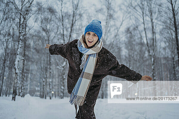 Cheerful mature woman standing with arms outstretched in snow at park