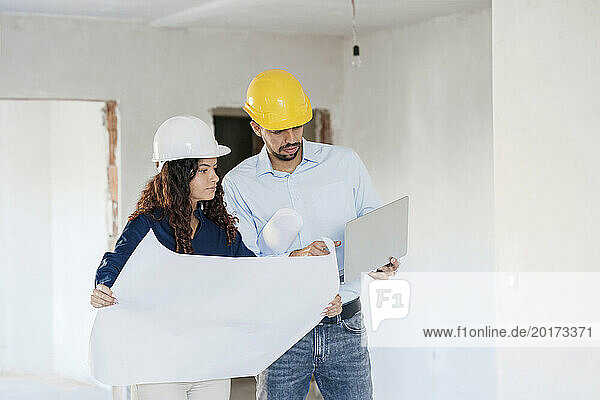 Architects with blueprint discussing over laptop at site