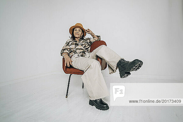 Carefree senior woman sitting on chair in front of white wall