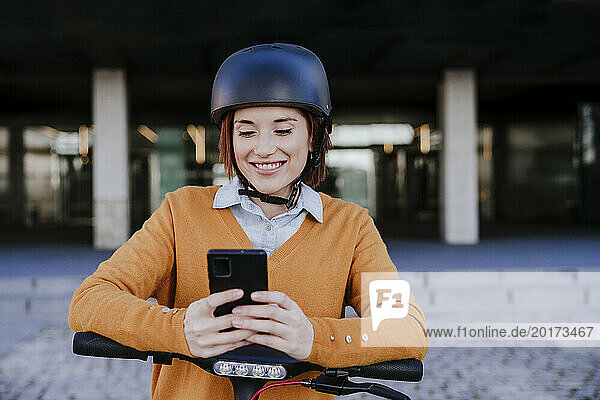 Smiling woman using smart phone near building