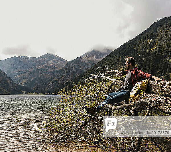 Young man sitting on fallen tree trunk near lake Vilsalpsee and mountains at Tyrol  Austria