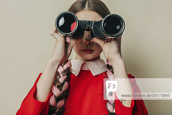 Young woman looking through binocular in front of wall