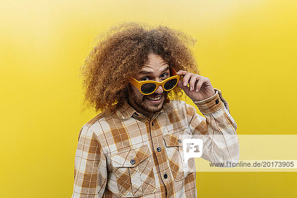 Happy man wearing sunglasses and standing in front of yellow wall