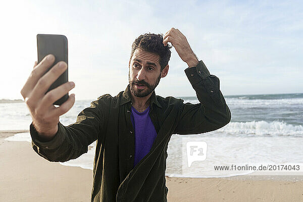 Man taking selfie through smart phone at beach on sunny day