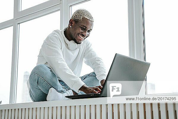 Smiling freelancer using laptop near window at home