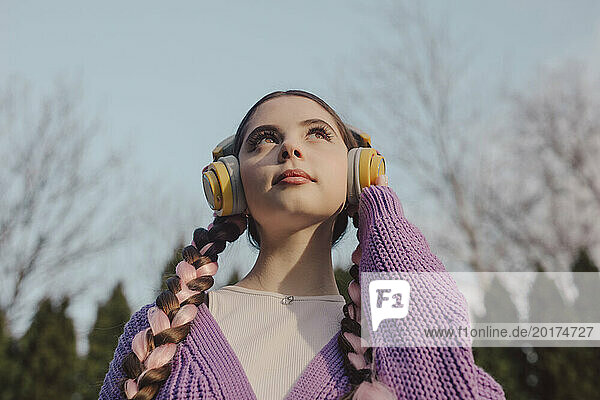 Young woman wearing wireless headphones listening to music under sky