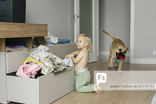 Shirtless girl removing clothes near drawer at home
