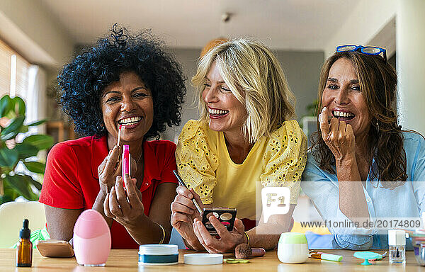 Laughing friends watching happy woman applying lipstick