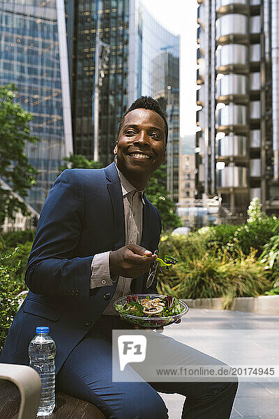Smiling mature businessman sitting with bowl of salad at office park