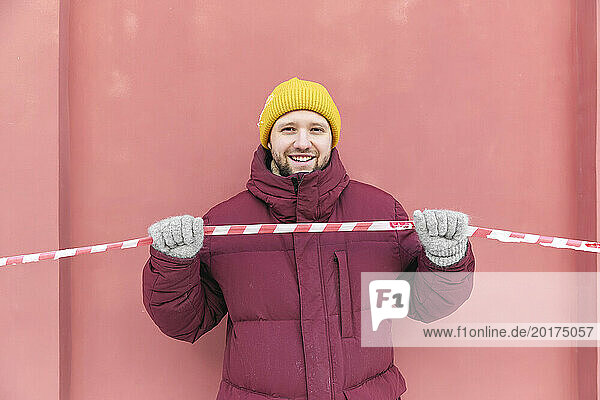 Happy man holding red and white barricade tape in front of peach wall