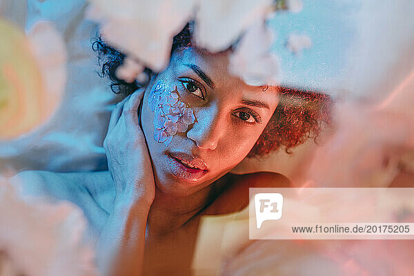 Beautiful woman lying below glass surface with flowers under neon lights