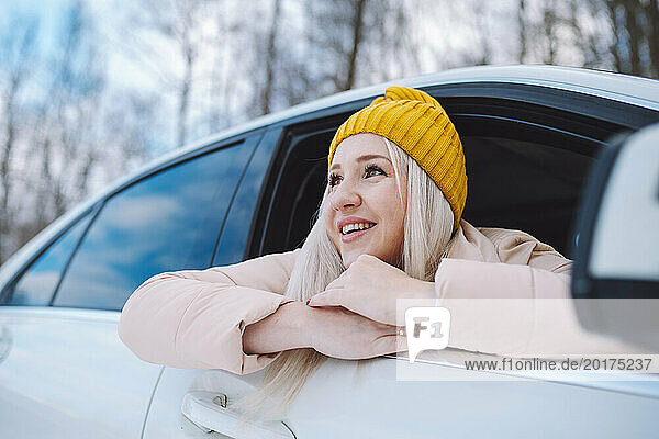 Happy woman leaning out of car window in winter forest