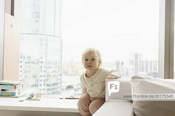Little girl sitting on window sill at home