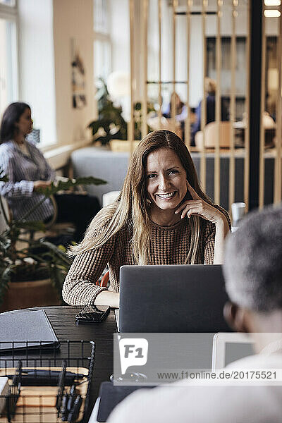 Portrait of smiling businesswoman sitting with laptop at desk in office