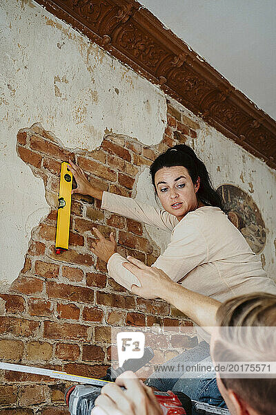 Man assisting woman in measuring brick wall while renovating home